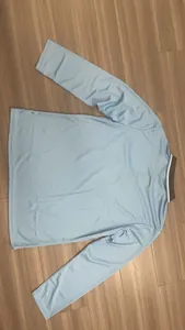 Vista posteriore di una polo a maniche lunghe azzurra distesa su pavimento in legno.