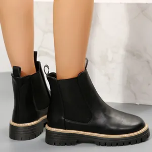 Vista lateral de botines Chelsea negros con suela gruesa en una modelo.