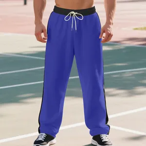 Detail view of men's blue wide-leg sweatpants with black side stripes worn on a model outdoors.