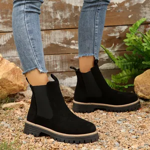 Botines Chelsea de ante negro con suela de plataforma gruesa en un entorno exterior.