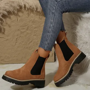 Primer plano de botines Chelsea de ante marrón con suela gruesa negra y pantalones vaqueros.