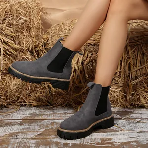 Vista detallada de botas Chelsea de ante gris con suelas de plataforma sobre fondo de heno rústico