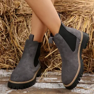 Primer plano de botas Chelsea de ante gris con suela gruesa en un entorno rústico.