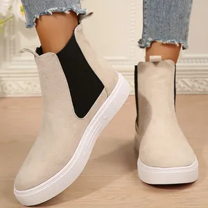 Primer plano de botas Chelsea beige con suelas blancas gruesas y elásticos negros laterales.