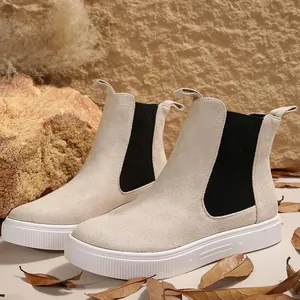 Botines Chelsea de ante beige con suelas blancas gruesas en un entorno natural.
