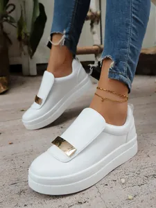 Close-up of stylish white platform slip-on sneakers with gold metal plate detail