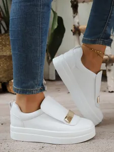 Close-up detail of stylish white platform slip-on sneakers featuring a gold metallic bar