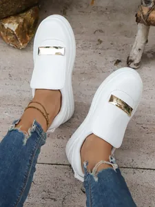 Macro view of white women's platform slip-on shoes with gold metallic bar detail