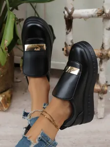 Close-up detail of women's black platform slip-on loafers with metallic gold bar accent