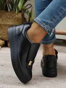 Close-up detail of stylish black platform slip-on shoes with metallic accent worn with blue jeans