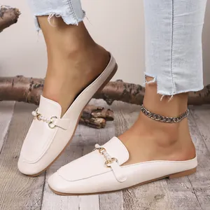 Detalle de mules beige con elegante hebilla de perlas metálicas y punta cuadrada