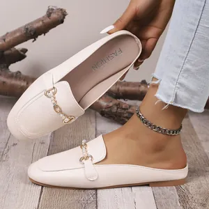 Detalle de primer plano de zuecos beige con hebilla dorada y cadena de perlas