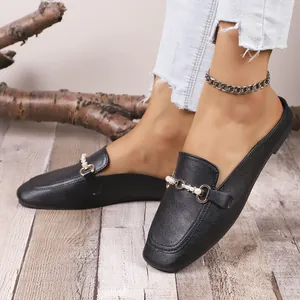 Detalle de mules de cuero negro con hebilla metálica y perlas de estilo elegante