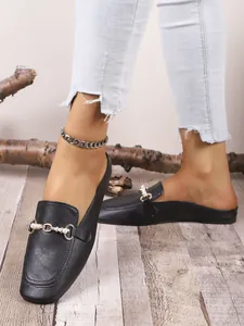 Primer plano de mocasines destalonados negros con hebilla metálica y detalle de perlas.