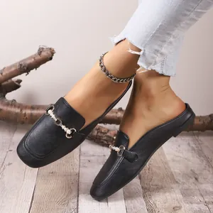 Vista detallada de elegantes mules negros con hebilla de perlas y metal sobre un suelo de madera