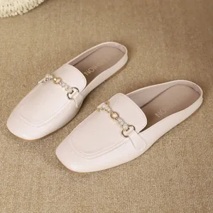 Detalle de elegantes mules crema con hebilla metálica decorativa y perlas falsas
