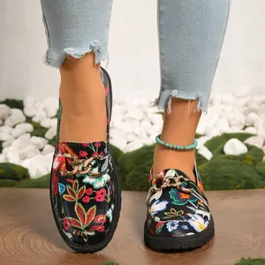 Vista detallada de mocasines negros de mujer con motivos florales y cadena dorada