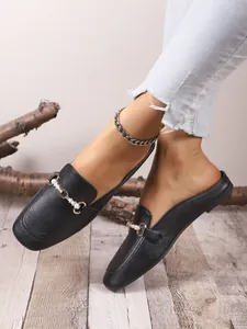 Elegantes mules negras de punta cuadrada con hebilla metálica y perlas en suelo de madera
