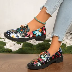 Detalle de mocasines negros con bordado floral y cadena dorada de plataforma