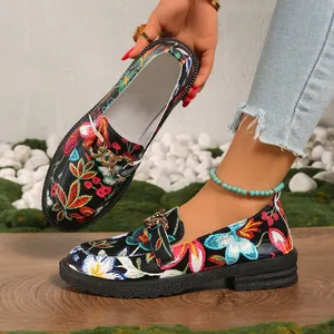 Vista detallada de mocasines bordados con flores, cadena dorada y suela negra gruesa
