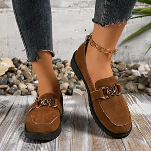 Detalle de mocasines de ante marrón con adorno de cadena dorada y suela gruesa de mujer
