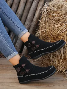 Detail of black flat ankle boots with decorative buttons and white contrast stitching.