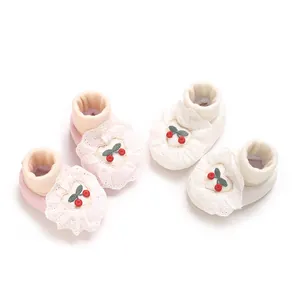 Detailed view of soft infant shoes with cherry embroidery and lace ruffles in pink and white.