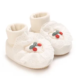 Macro detail of soft white baby sock shoes with lace trim and red cherry embroidery
