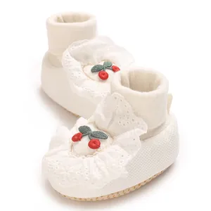 Close-up of white baby sock-shoes with lace trim and cherry embroidery details