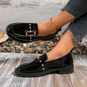 Primer plano de mocasines de charol negro con hebilla metálica decorativa