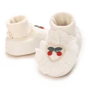 Detailed macro view of white infant sock shoes with lace ruffles and cherry embroidery