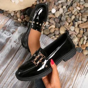 Primer plano de mocasines negros de charol con hebilla dorada y suela gruesa.