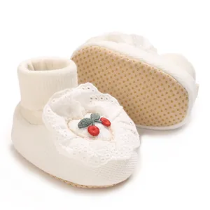 Detailed view of soft white newborn baby booties featuring cherry embroidery and lace trim