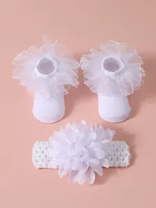 Detalle de calcetines blancos de encaje para bebé y diadema con flor grande a juego