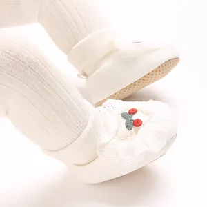 Close-up of soft white baby booties with lace trim and cherry embroidery detail