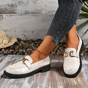 Primer plano de mocasines blancos con cadena dorada y patrón texturizado