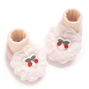Detailed view of pink newborn baby booties with lace ruffles and cherry embroidery