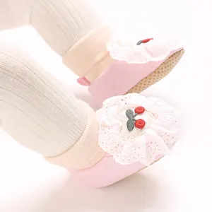Close-up of pink baby girl sock shoes with delicate lace ruffles and cherry embroidery.