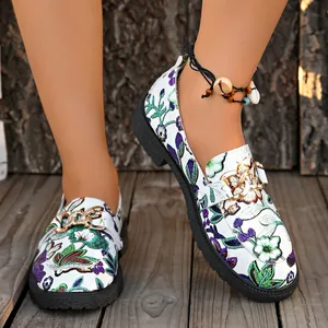 Detalle de mocasines blancos bordados con flores y una elegante cadena de color dorado