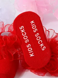 Detalle de calcetines de princesa rojos con volantes de encaje y suela antideslizante.