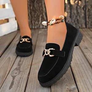 Detalle de mocasines de gamuza negra con cadena dorada y suela gruesa sobre madera.
