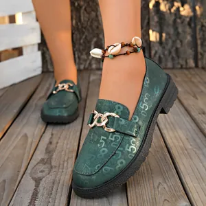 Vista detallada de mocasines verdes estampados con cadena dorada y suela gruesa