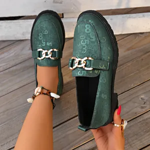 Detalle de mocasines verde oscuro con números grabados y hebilla de cadena dorada.