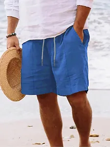 Detailed view of men's blue linen beach shorts with drawstring worn by model on sandy shore