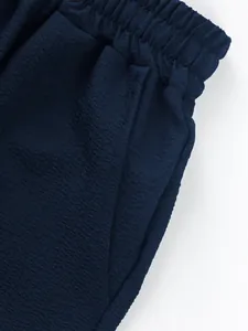 Close-up detail of navy blue textured fabric shorts with elastic waistband and pocket.