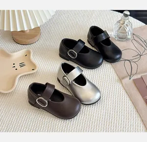 Selection of girls' Mary Jane shoes in black, silver and brown on a textured surface.