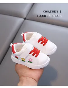 Weiße Kleinkinder-Sneaker mit roten Schnürsenkeln und Blumenstickerei auf grau