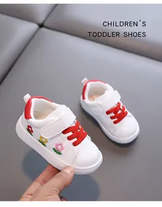 Detailansicht weißer Kleinkindschuhe mit Blumenstickerei und roten Schnürsenkeln.