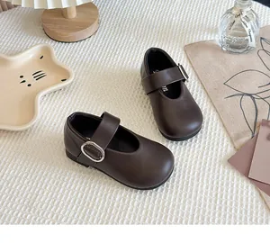 Close-up of dark brown girl's Mary Jane leather shoes with buckle straps on a white background.