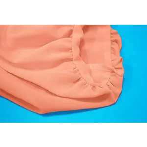 Gros plan sur l'ourlet élastique et les coutures d'un cache-maillot en mousseline corail.